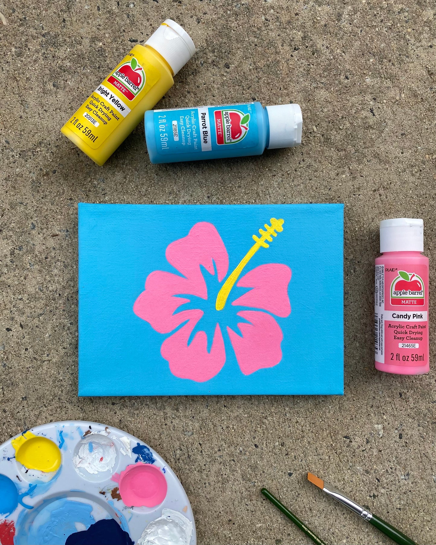 Amber Peeks Art: Painting of a pink flower with a blue background outside with art supplies surrounding it.