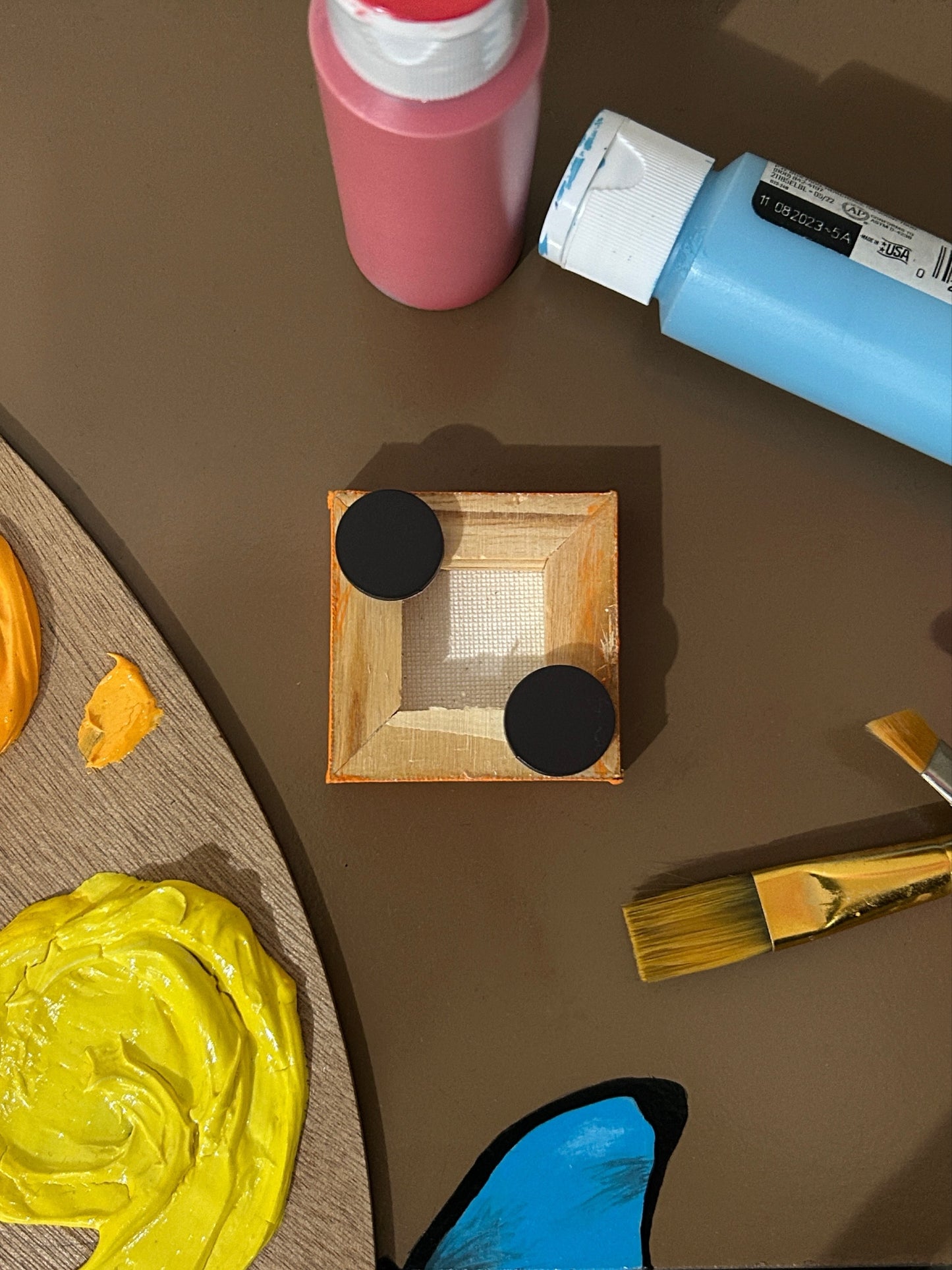 Amber Peeks Art: Small orange magnet with a pumpkin face design on a brown surface with art supplies.