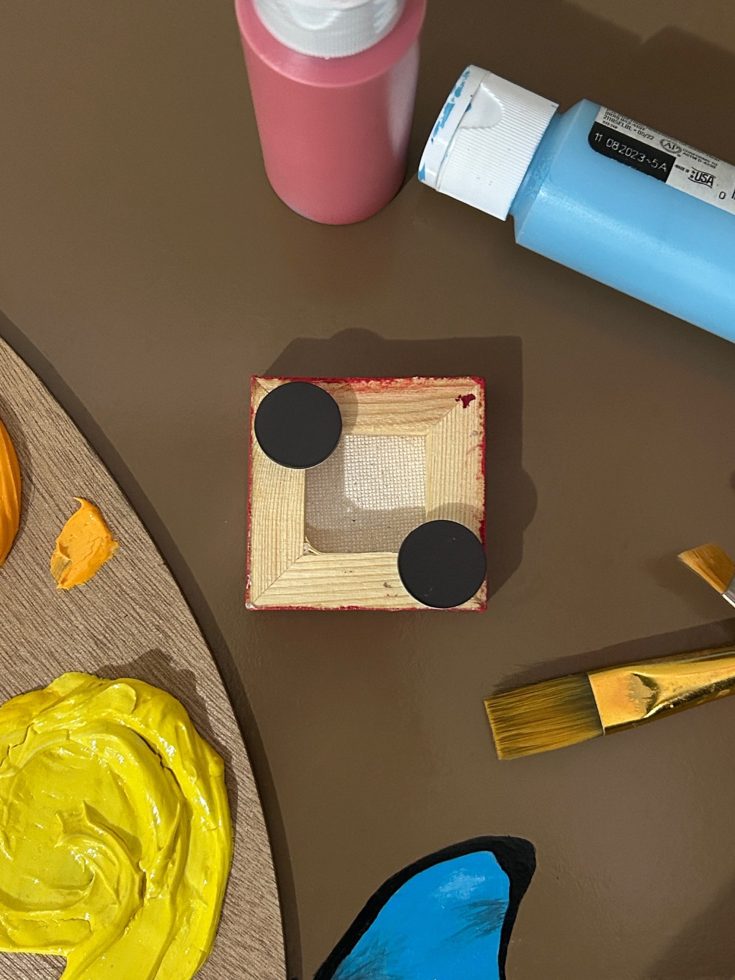 Amber Peeks Art: Small red magnet painted like a strawberry on a brown surface with art supplies.