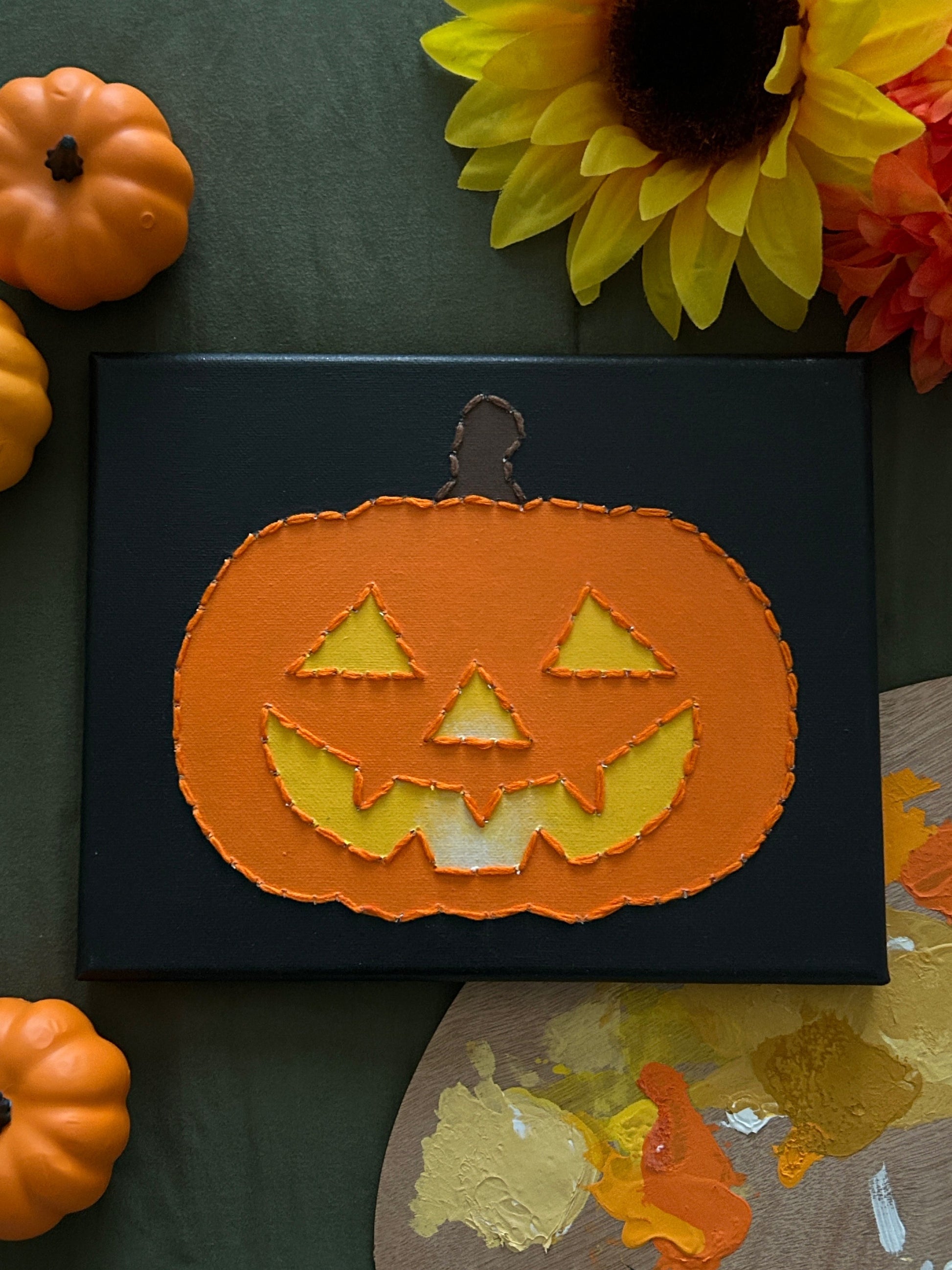 Amber Peeks Art: Pumpkin face decoration on a black background with pumpkins and sunflowers around