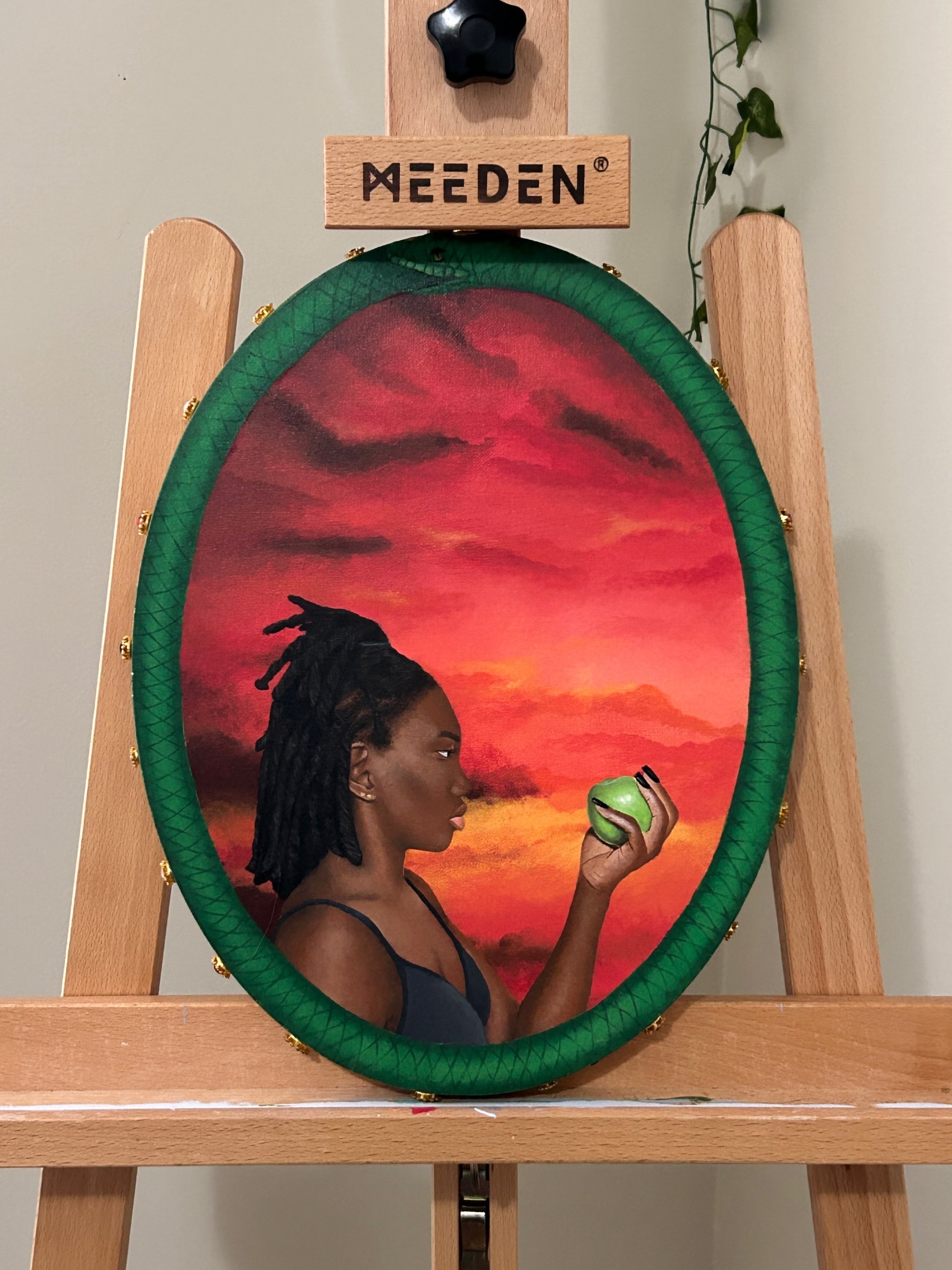 Amber Peeks Art: Artistic depiction of a woman holding a green apple against a sunset sky, displayed on an easel.