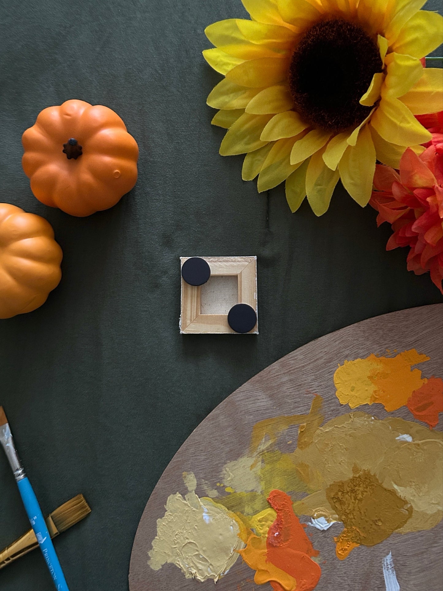 Amber Peeks Art: Small white ghost magnet on a dark surface with pumpkins, sunflowers, and a paint palette.