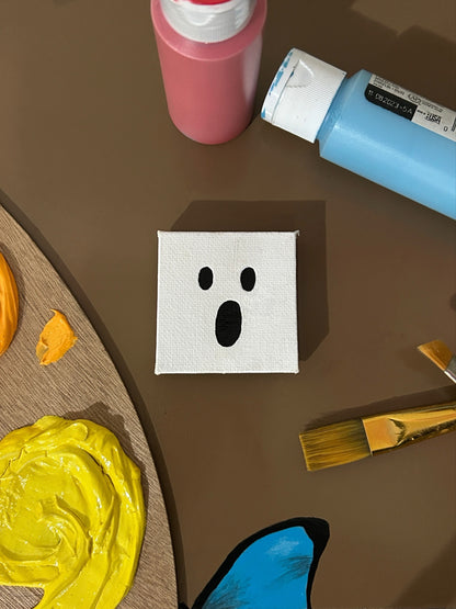 Amber Peeks Art: Small white ghost magnet on a dark surface with pumpkins, sunflowers, and a paint palette.