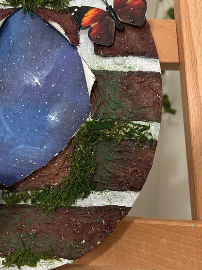 Amber Peeks Art: Painting with a blue celestial design, greenery, and a butterfly on a wooden easel. 