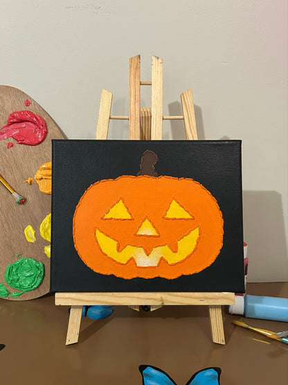 Amber Peeks Art: painting of a jack-o'-lantern on a small easel with art supplies in the background.