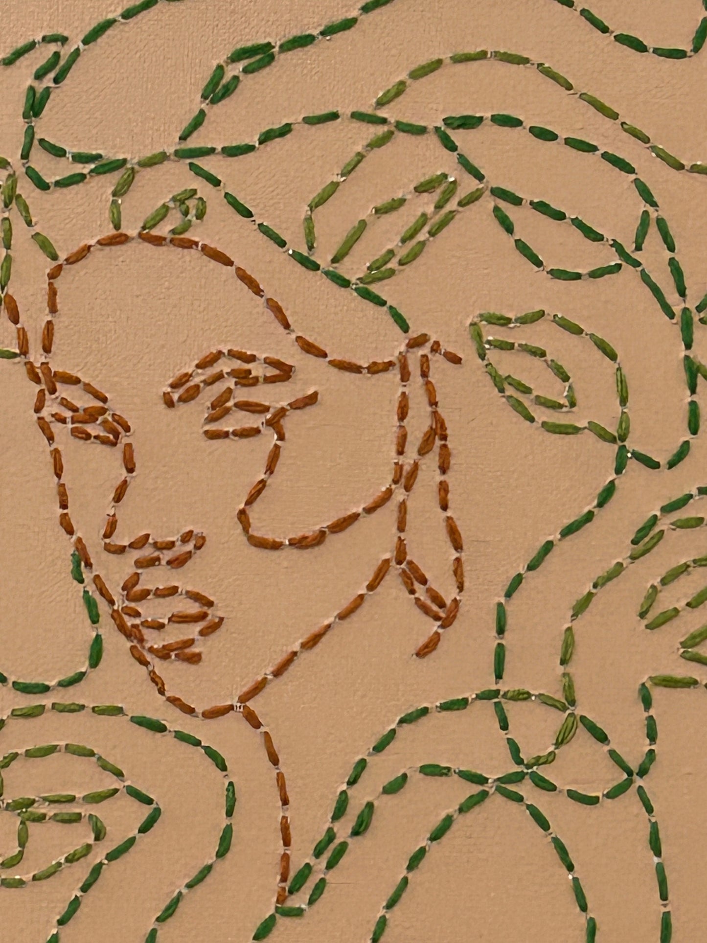 Amber Peeks Art: Embroidery of medusa with green thread on a beige canvas, displayed on a wooden easel.