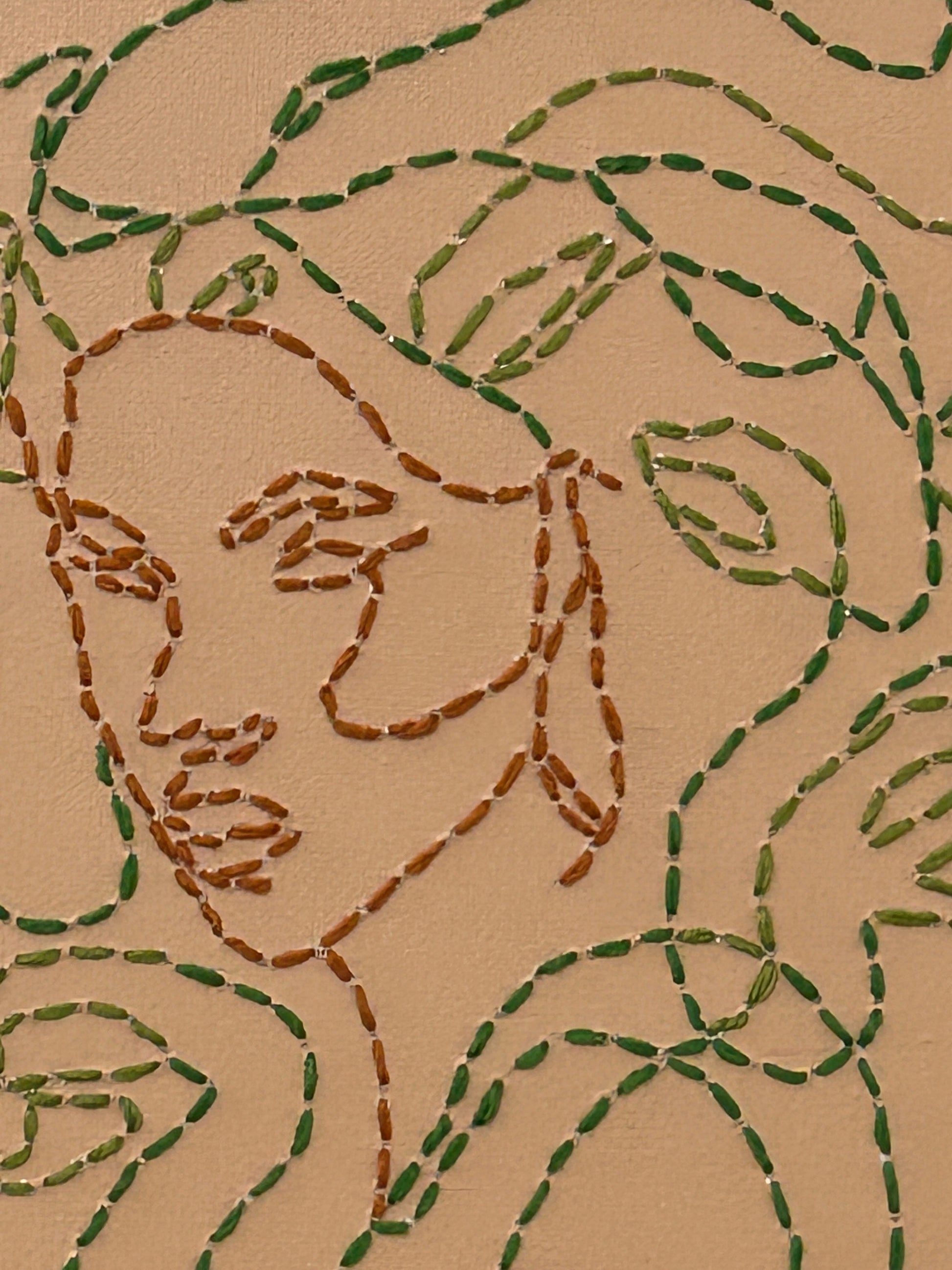Amber Peeks Art: Embroidery of medusa with green thread on a beige canvas, displayed on a wooden easel.