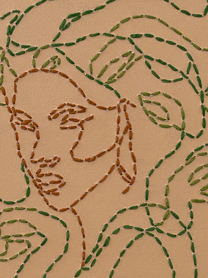 Amber Peeks Art: Embroidery of medusa with green thread on a beige canvas, displayed on a wooden easel.