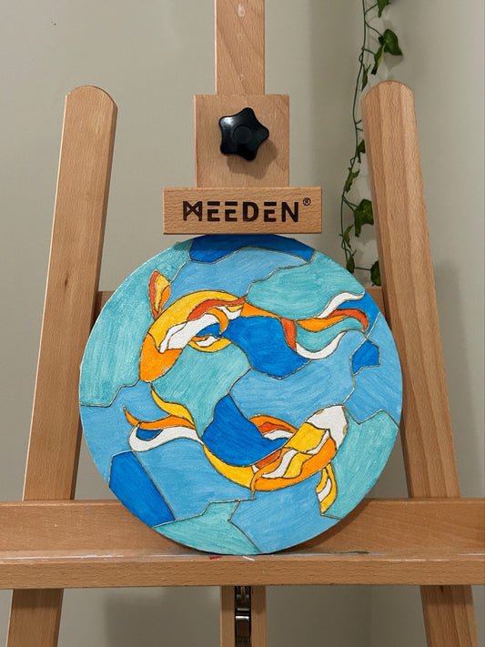 Amber Peeks Art: Wooden art easel with a round canvas painting featuring colorful fish designs on a blue background created by Atlanta multi-disciplinary visual artist Amber Peeks.