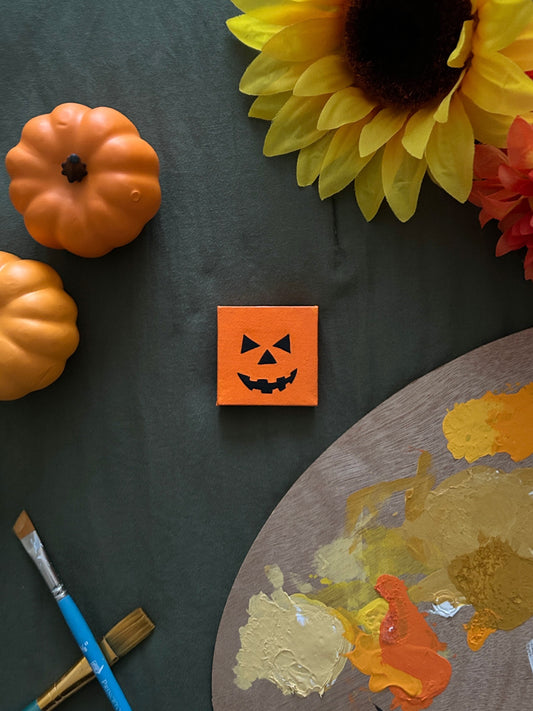 Amber Peeks Art: Small orange pumpkin magnet on a dark surface with pumpkins, sunflowers, and a paint palette.