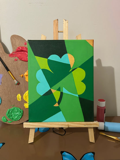 Amber Peeks Art: Green abstract painting of a shamrock on a small easel with art supplies in the background.